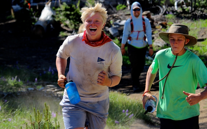 two students jog through grass and smile at the camera